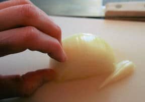 holding onion on cutting board with fingers folded back