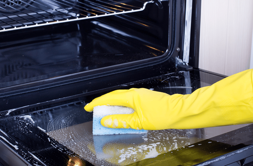Gloved hand holding sponge, cleaning oven glass