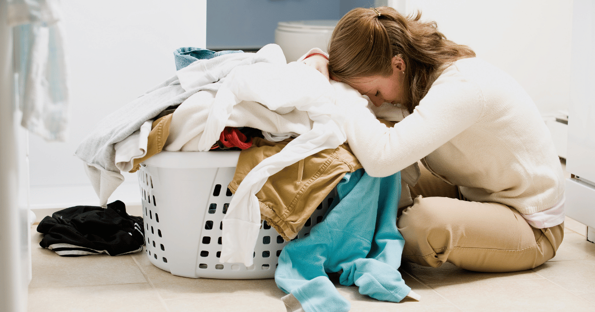 overwhelmed woman sitting on the floor with a basket of dirty laundry