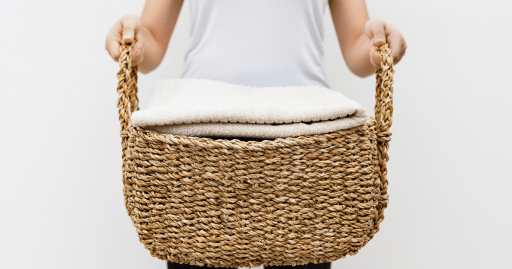 White background, woman holding woven laundry basket with cream colored towels cleaned with borax