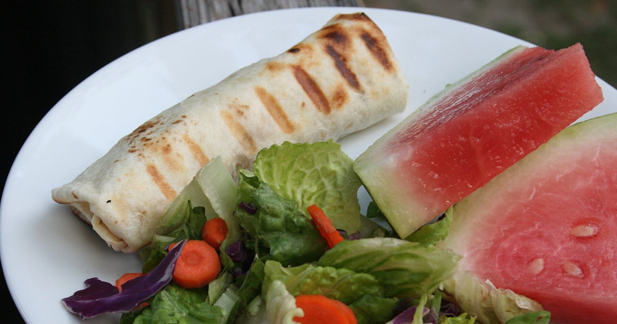 Grilled Chicken Burrito on a plate with a green salad and sliced watermelon