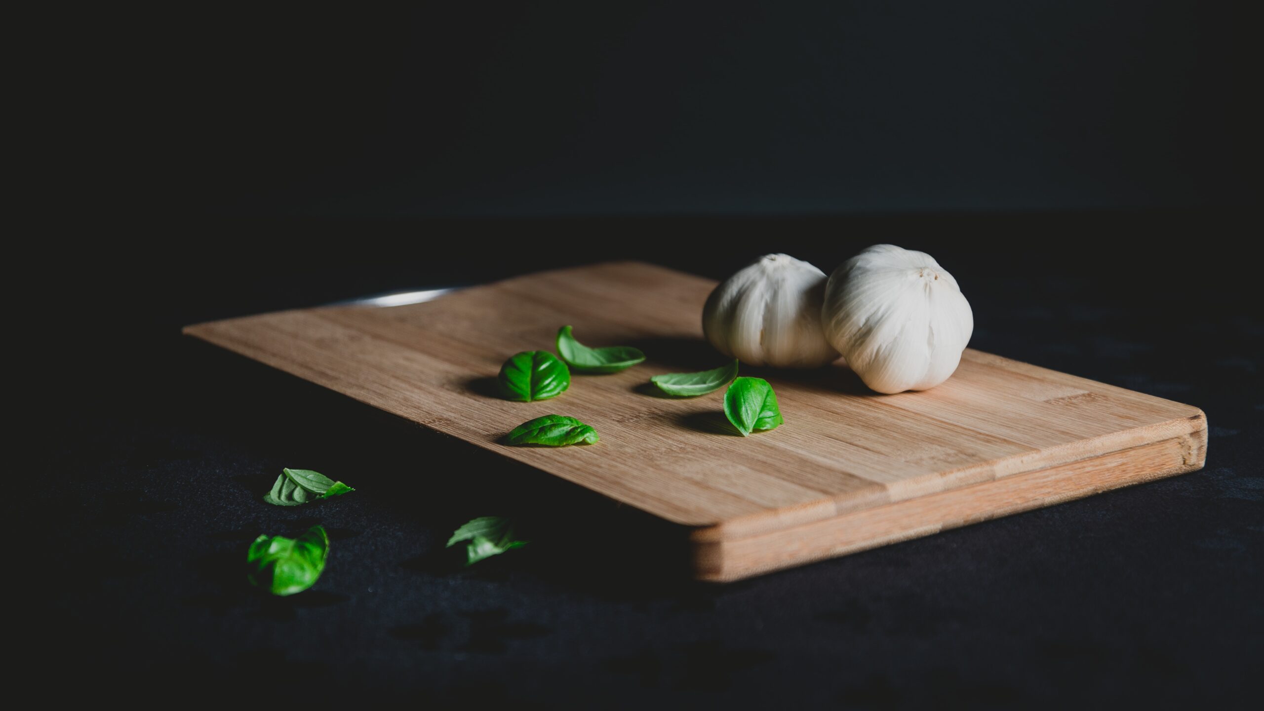 black background cutting board with garlic and green herbs on it