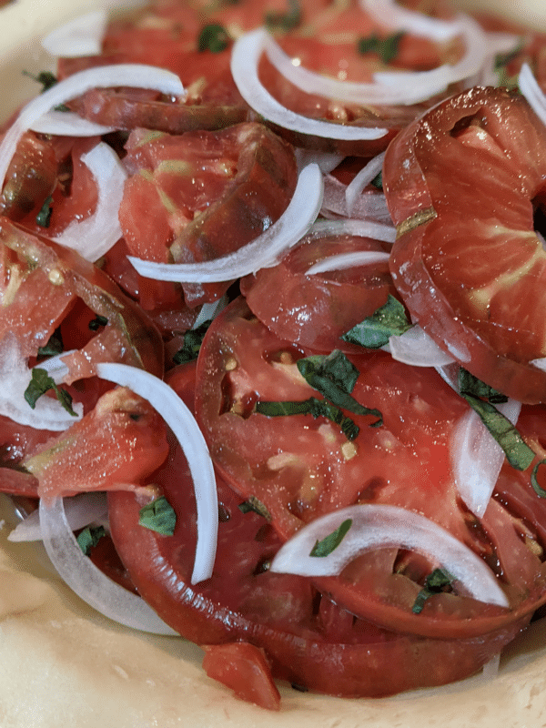 Close-up of an unbaked tomato pie showing sliced heirloom tomatoes, fresh basil, and thinly sliced onions