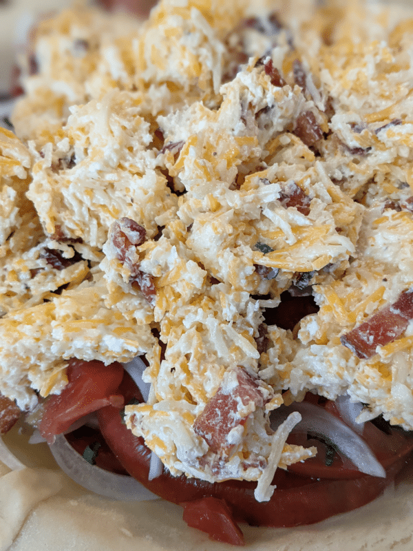 Close up of an unbaked tomato pie, showing the cheese and bacon mixture part of the filling.